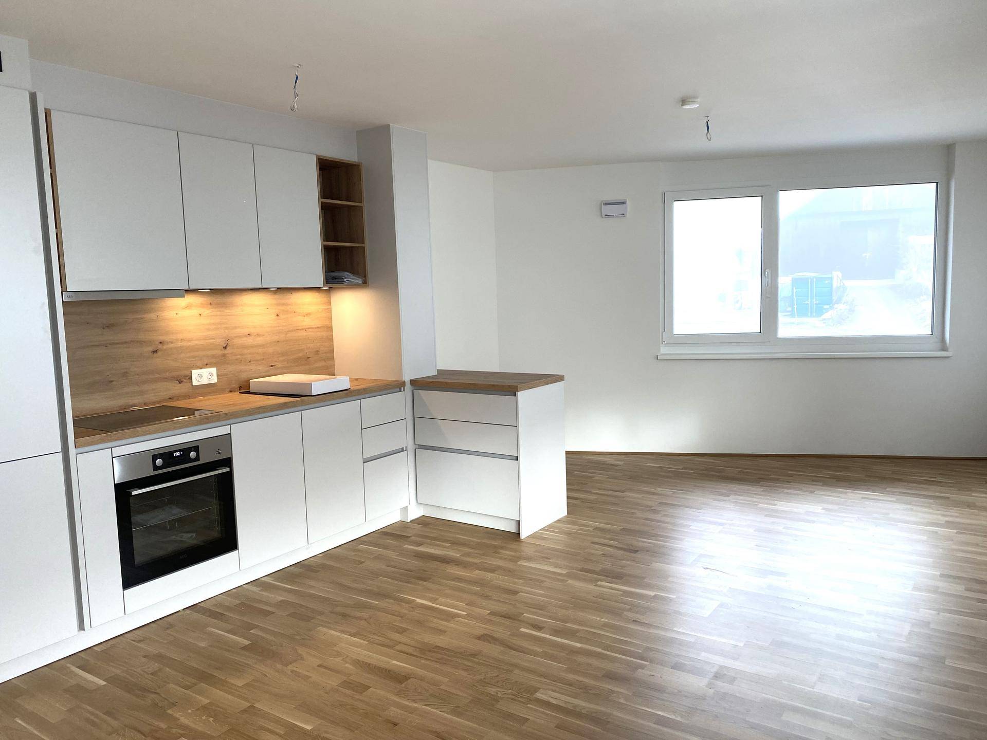 Helle, offene Küche mit modernen weißen Schränken und Holzdetails, angrenzend an einen geräumigen Wohnbereich mit Parkettboden.