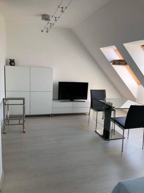 Heller Wohnbereich im Dachgeschoss mit Fernseher, modernem Esstisch und Dachfenstern.