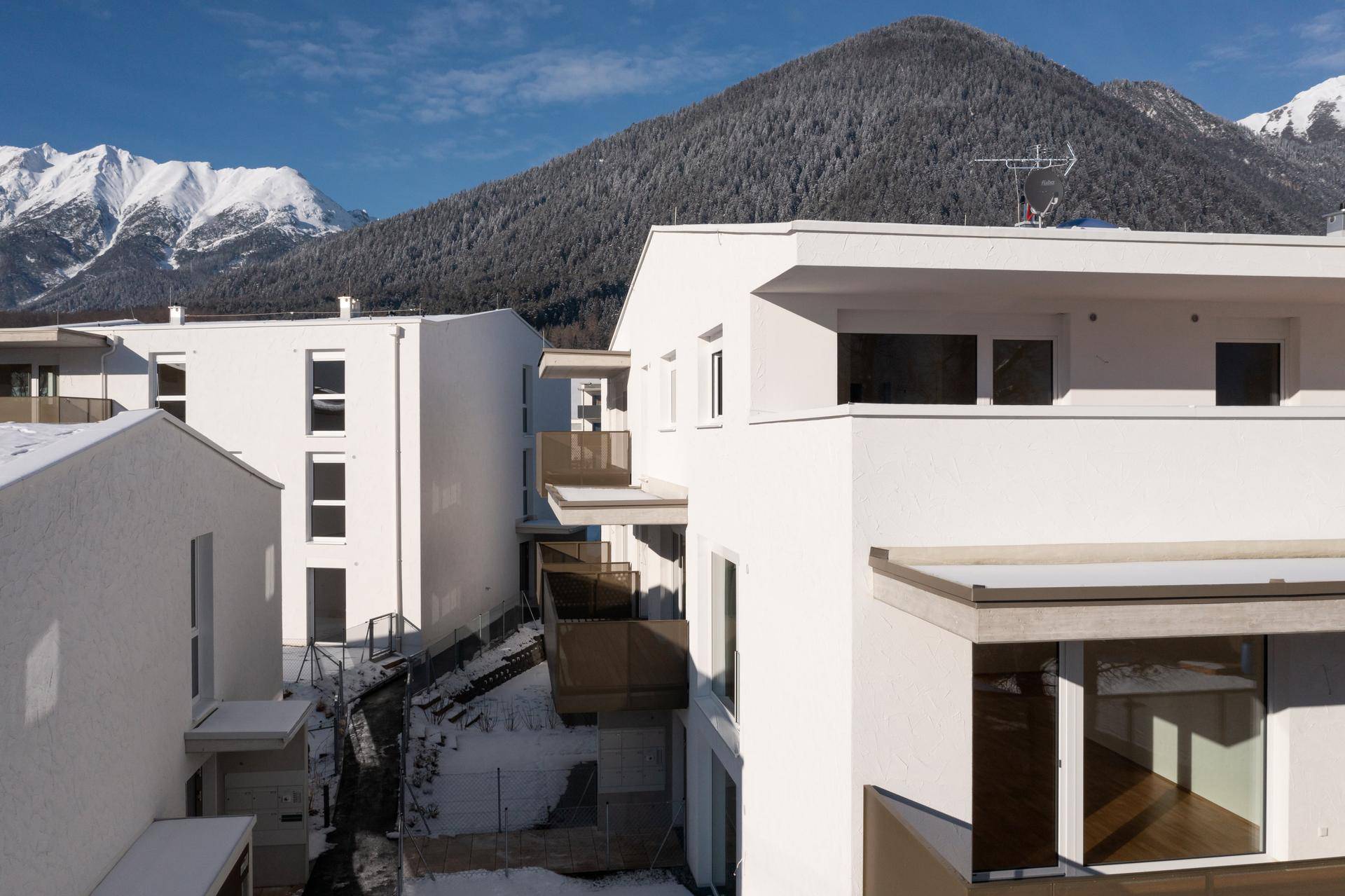 Moderne Wohngebäude mit Flachdächern und Balkonen vor einer Bergkulisse.