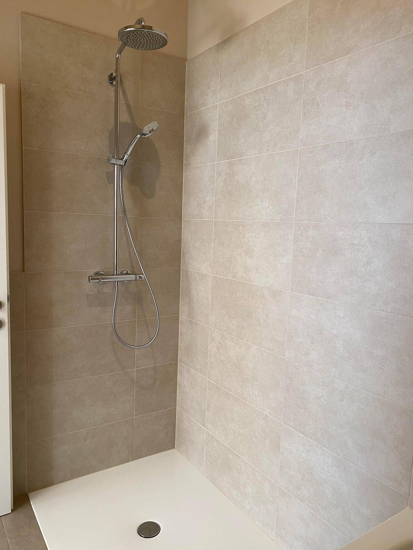Moderne Dusche mit Regenduschkopf und beigefarbenen Wandfliesen.
