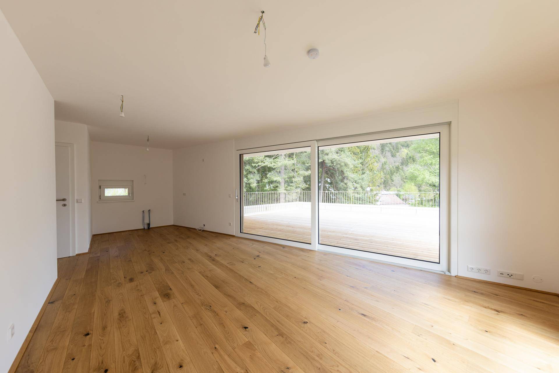 Leeres Wohnzimmer mit Eichenparkett und großen Schiebetüren zur Terrasse, bereit zum Einzug.