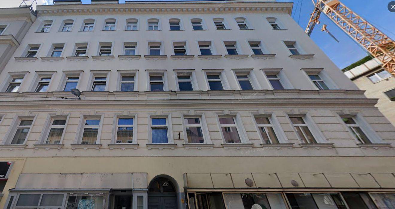 Klassische Fassade eines Mehrfamilienhauses mit vielen Fenstern und Geschäften im Erdgeschoss.