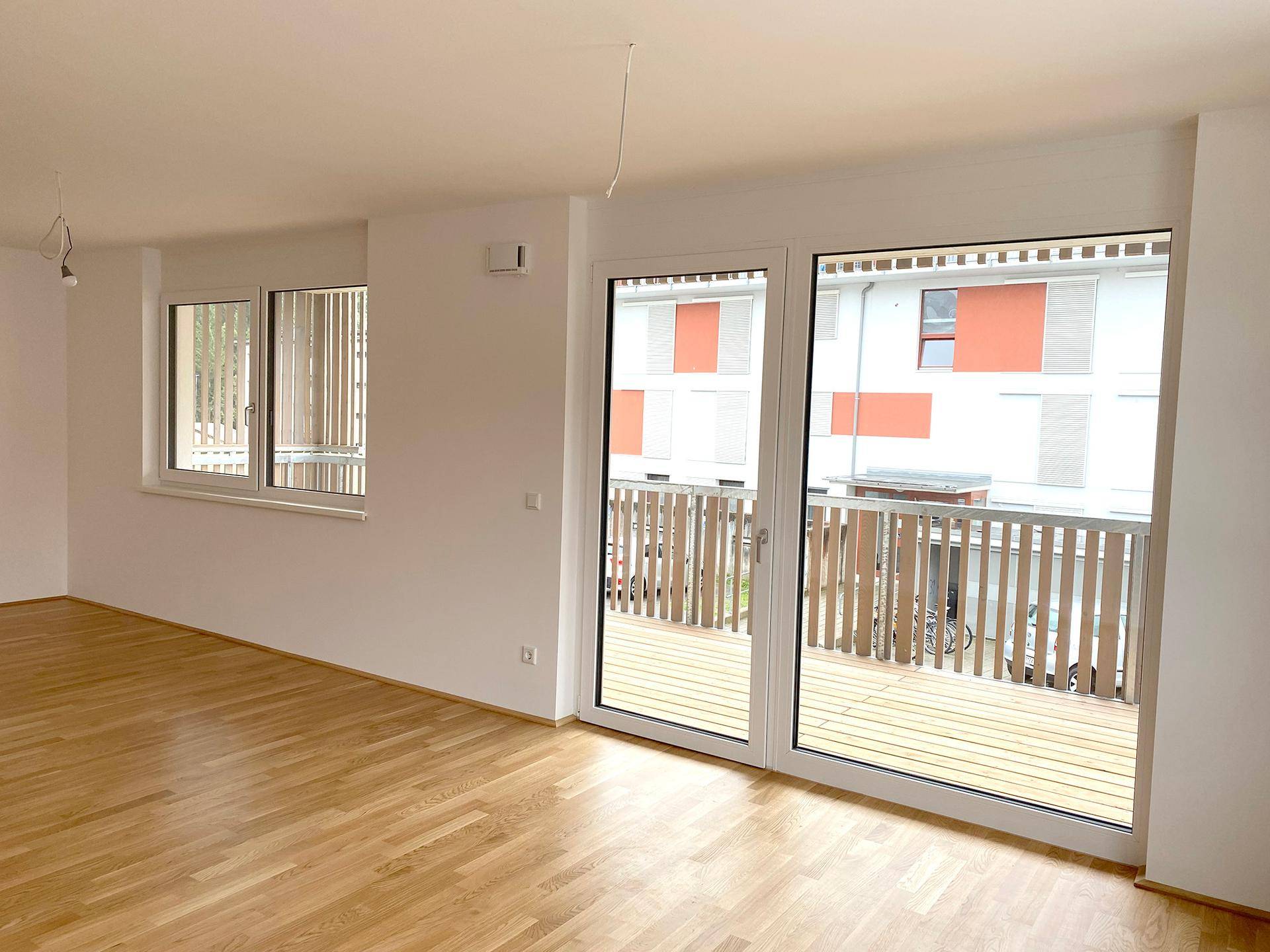 Heller Raum mit Eichenparkett, großen Fenstern und Zugang zu einem Balkon, ideal für einen Wohnbereich.