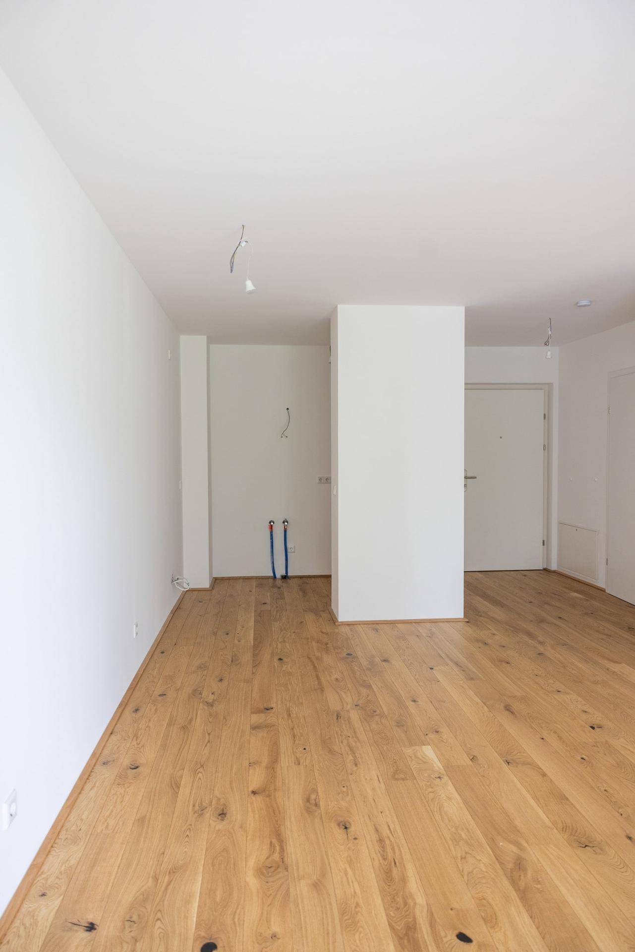 Leerer Küchenbereich mit Holzboden und Anschlüssen für eine zukünftige Einbauküche.