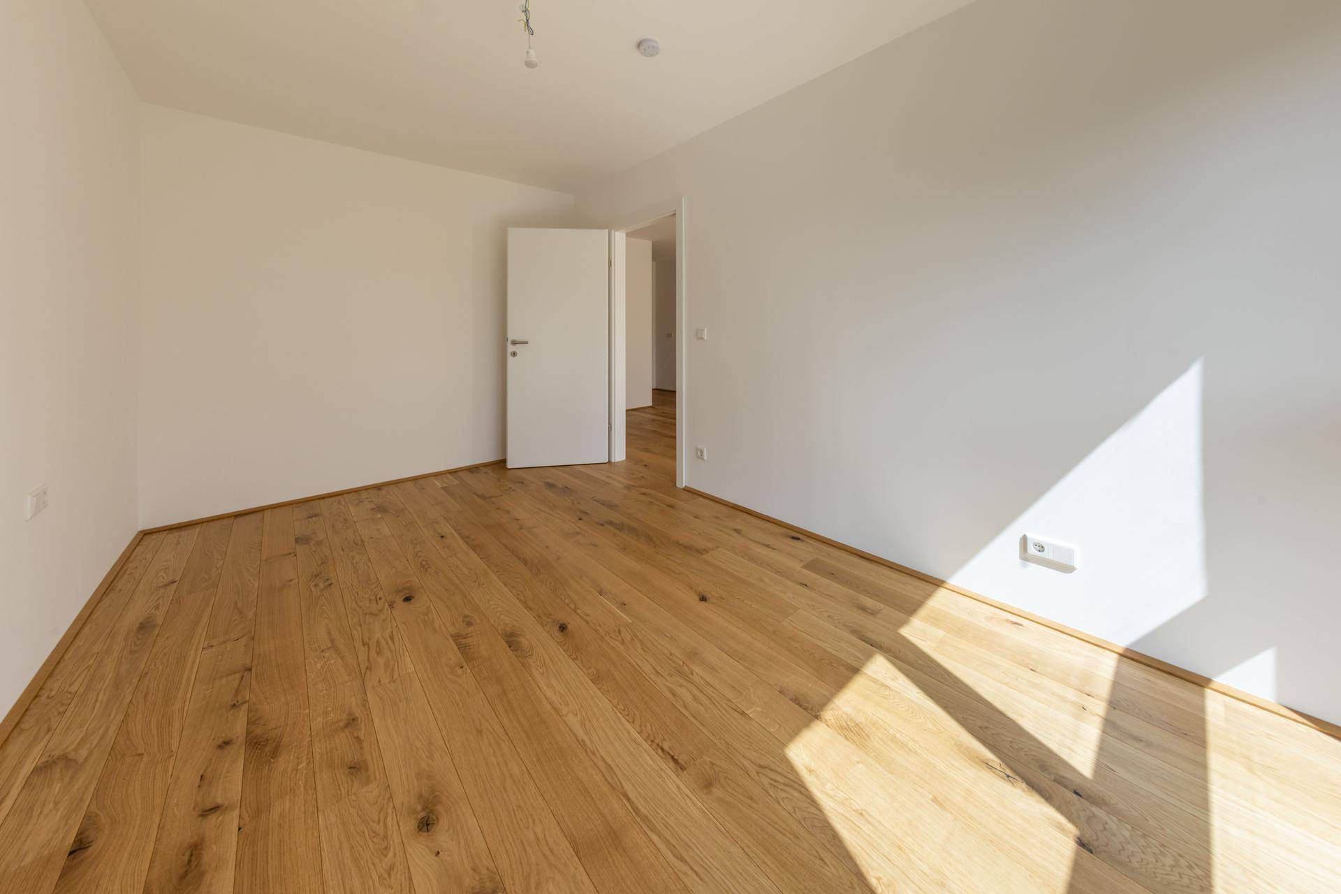 Geräumiger, heller Raum mit Holzboden und Zugang zu weiteren Zimmern.