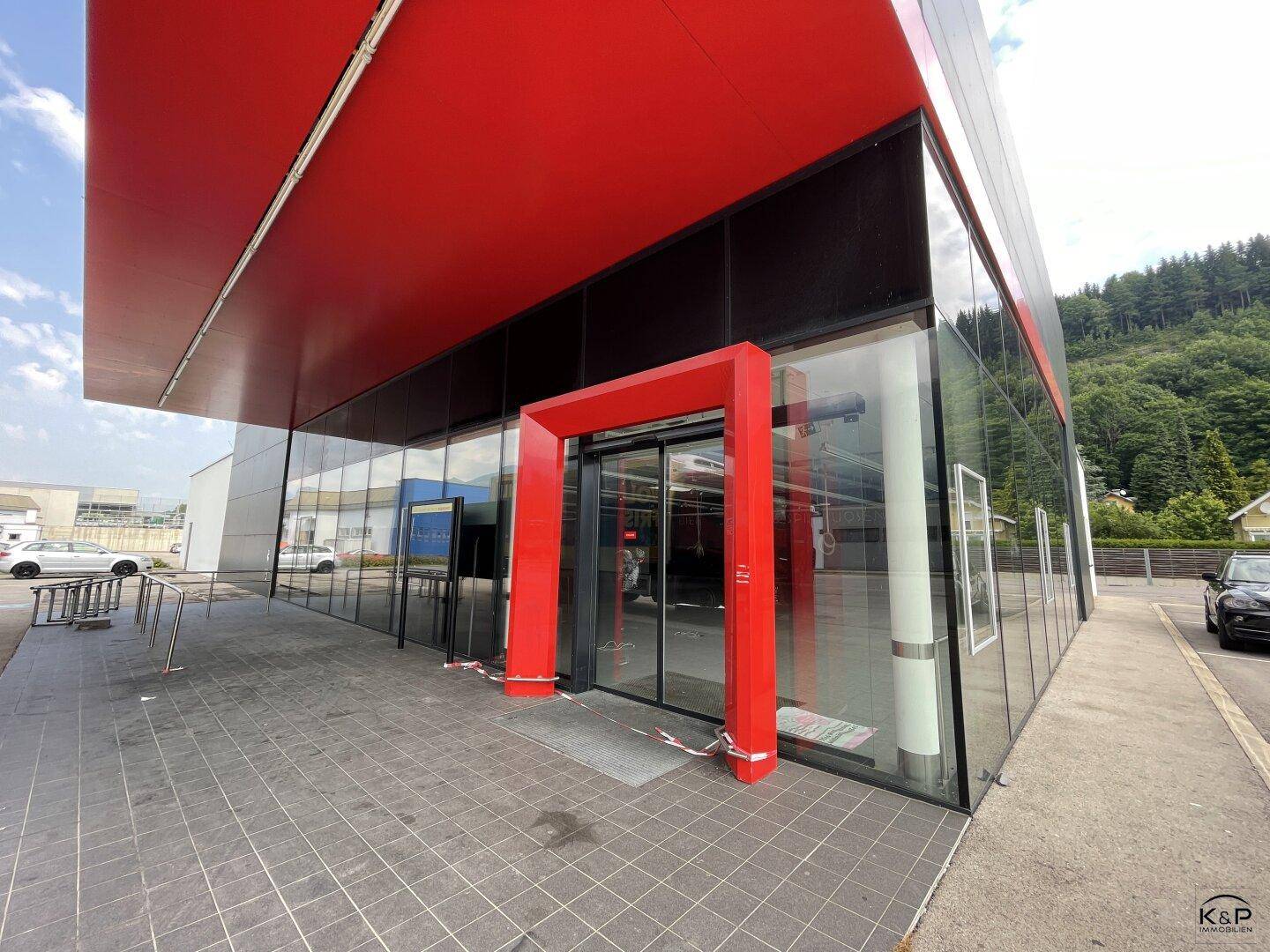 Eingangsbereich eines modernen Geschäftsgebäudes mit rotem Rahmen und breiter Glasfront.