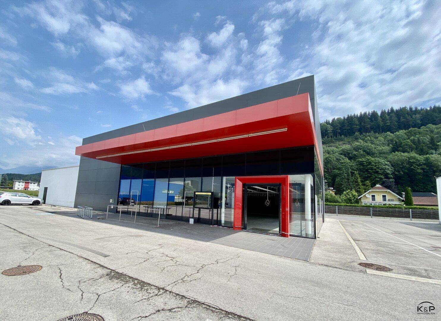 Moderne Geschäftsfassade mit rotem Vordach und großen Glasflächen unter blauem Himmel.