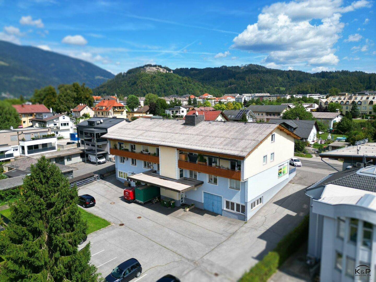 Luftaufnahme des Gebäudes mit Parkplätzen und grüner Umgebung unter blauem Himmel.