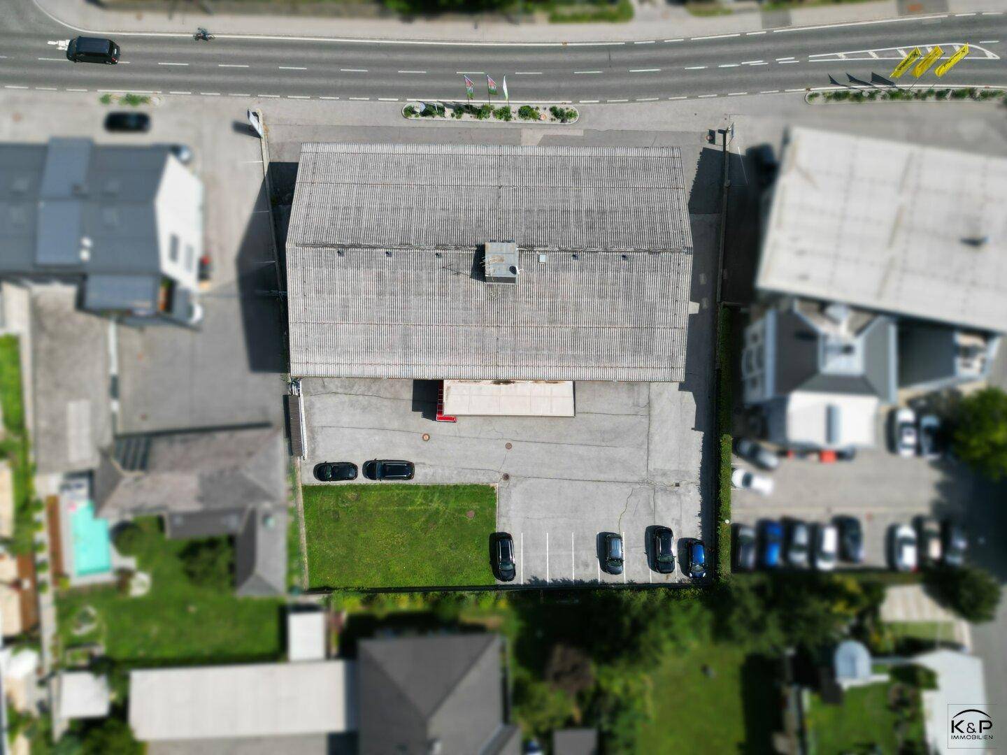 Senkrechte Luftaufnahme des Gebäudes mit Dach, Parkplätzen und angrenzender Grünfläche.