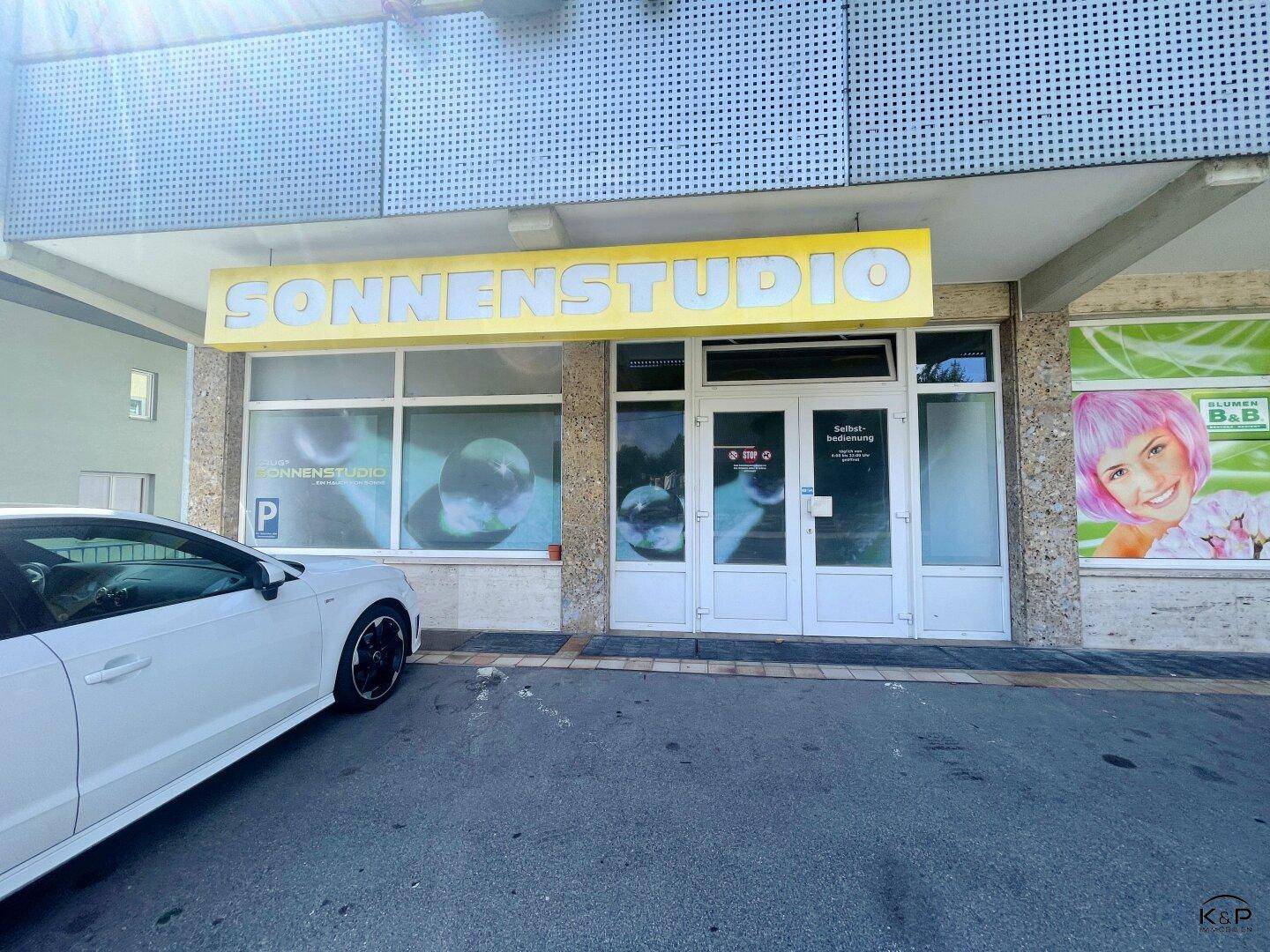Eingangsbereich eines Sonnenstudios mit großer Beschilderung und Parkplatz direkt davor.