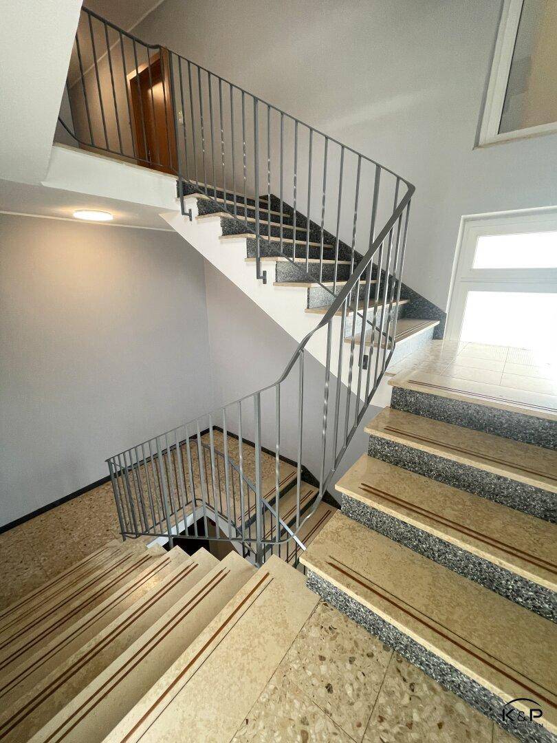 Treppenhaus mit Terrazzoboden und Metallgeländer, das zu den oberen Etagen führt.