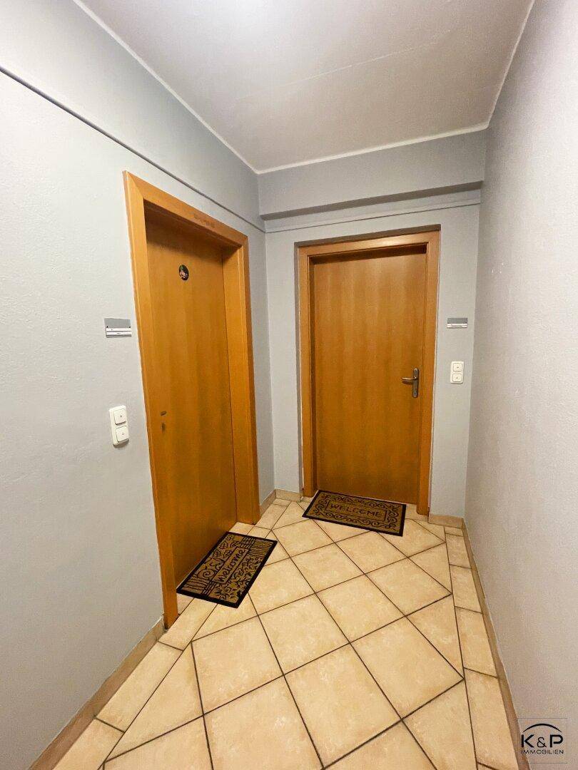 Heller Flur mit zwei Holztüren und beigefarbenen Fliesen auf dem Boden.