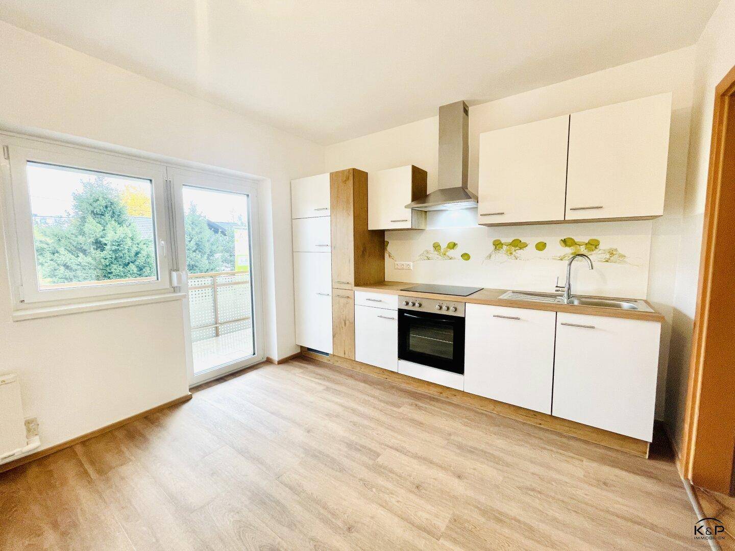 Moderne Einbauküche mit weißen Schränken, Holzelementen und Zugang zum Balkon.