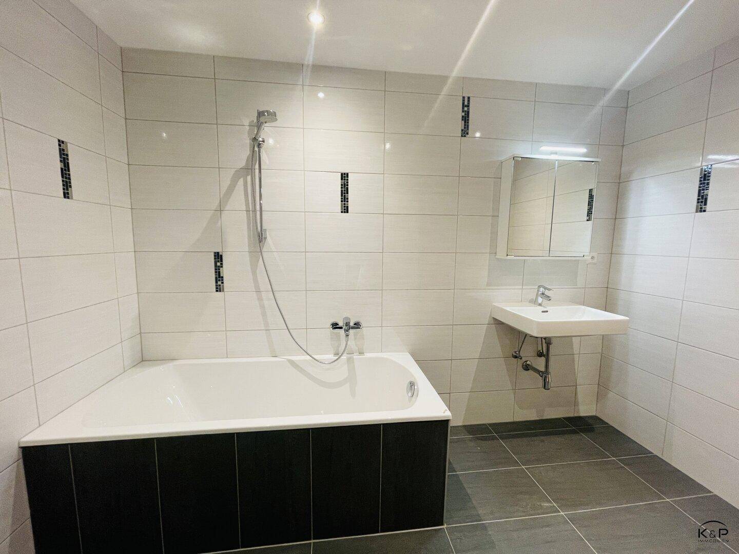 Helles Badezimmer mit Badewanne, Waschbecken und Spiegelschrank über dem Waschtisch.