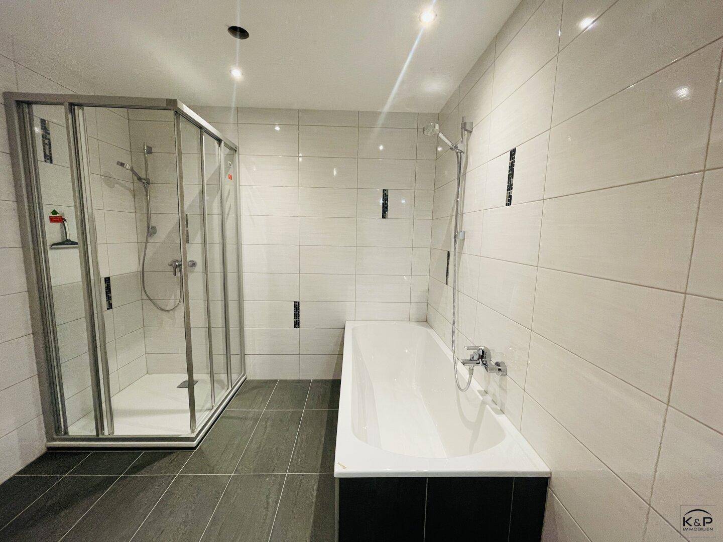 Modernes Badezimmer mit Badewanne, Duschkabine und großen weißen Fliesen.