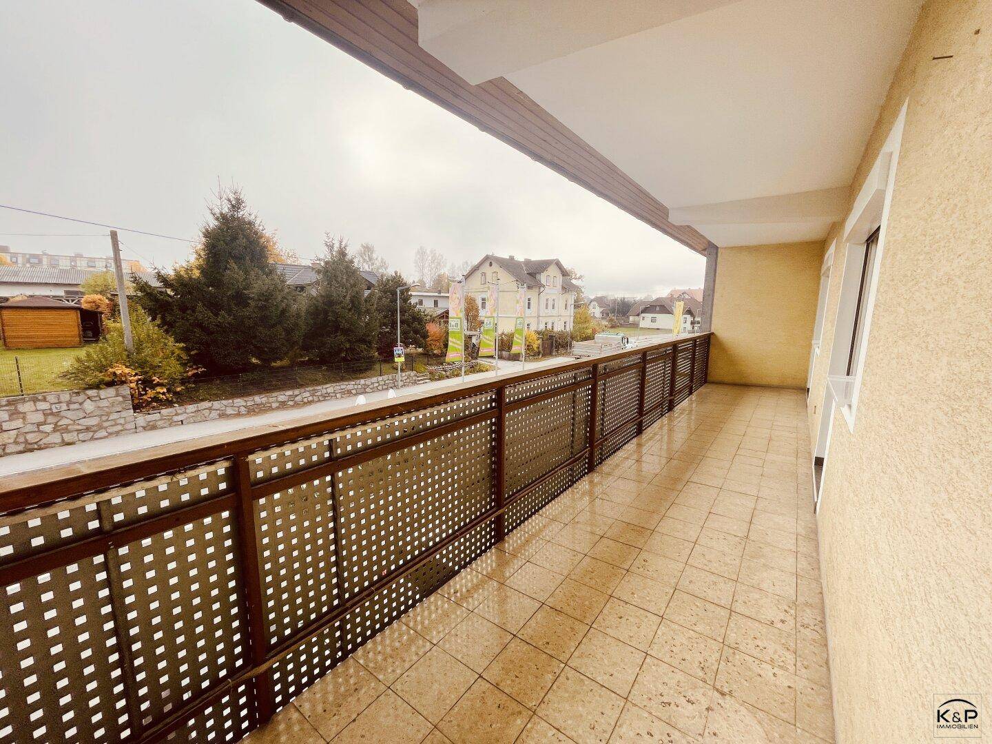 Langer Balkon mit Fliesenboden und Blick auf die Straße und umliegende Gebäude.