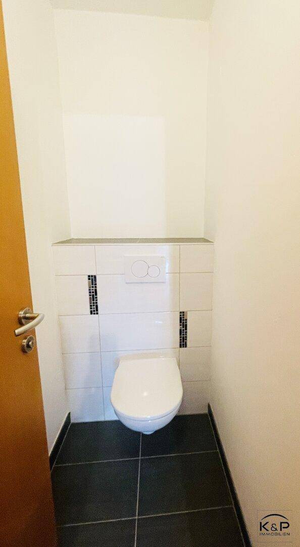 Separates WC mit wandhängender Toilette und modernen Fliesen an der Wand.
