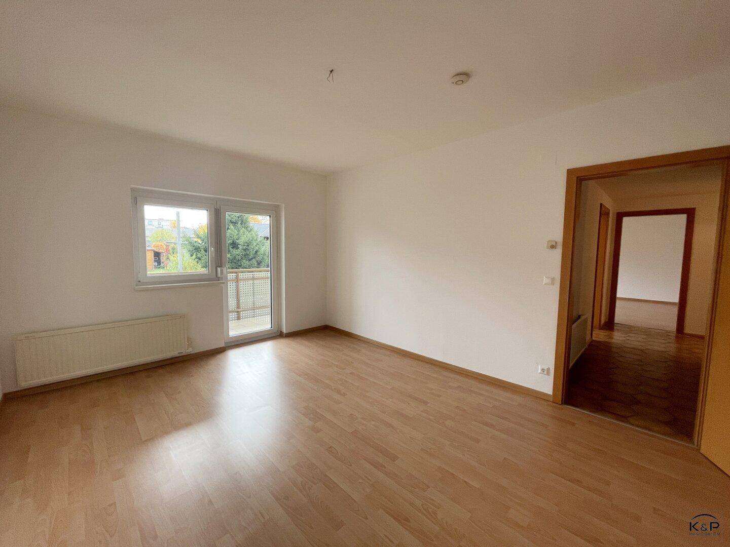 Geräumiges Wohnzimmer mit Laminatboden und Zugang zu einem kleinen Balkon.