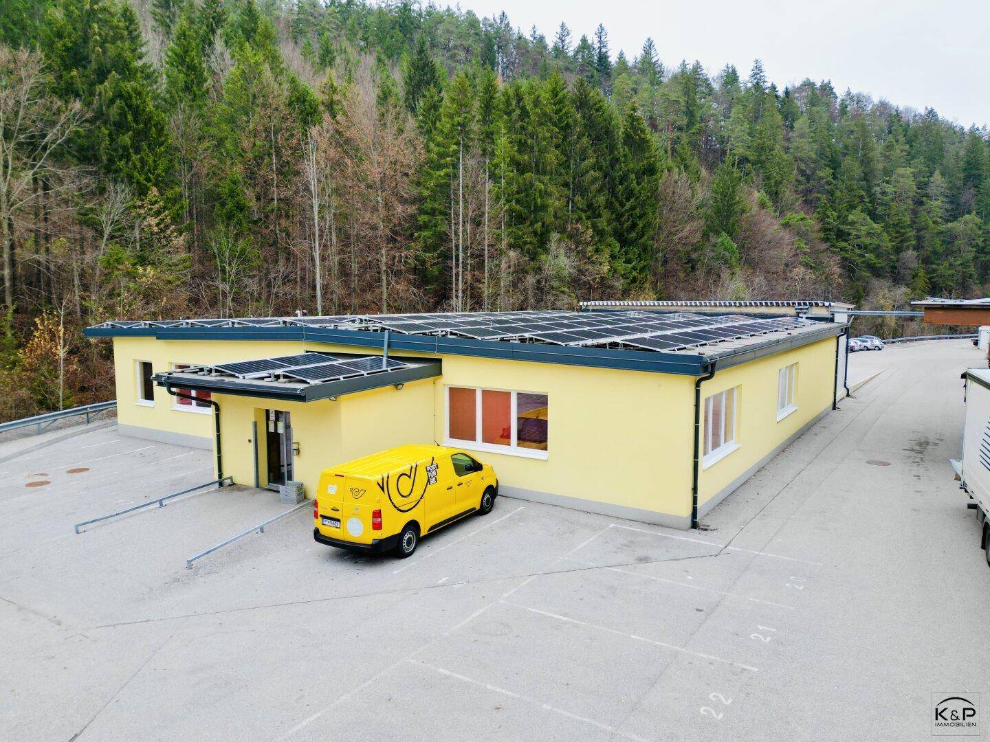 Helles, gelbes Geschäftsgebäude mit Solarpaneelen auf dem Dach und einem Lieferwagen auf dem Parkplatz.