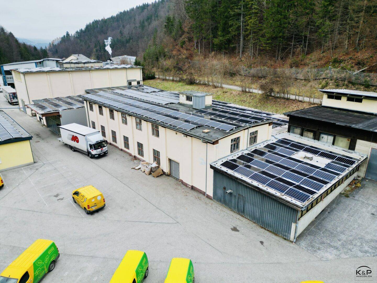 Industrielle Anlage mit verschiedenen Gebäuden, Solaranlagen und Lieferfahrzeugen auf dem Gelände.
