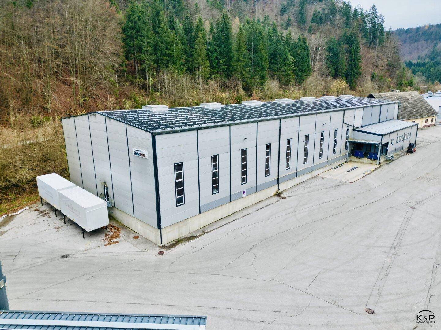 Großes, modernes Industriegebäude mit Metallfassade und hohen Fenstern, umgeben von einer weiten Freifläche.