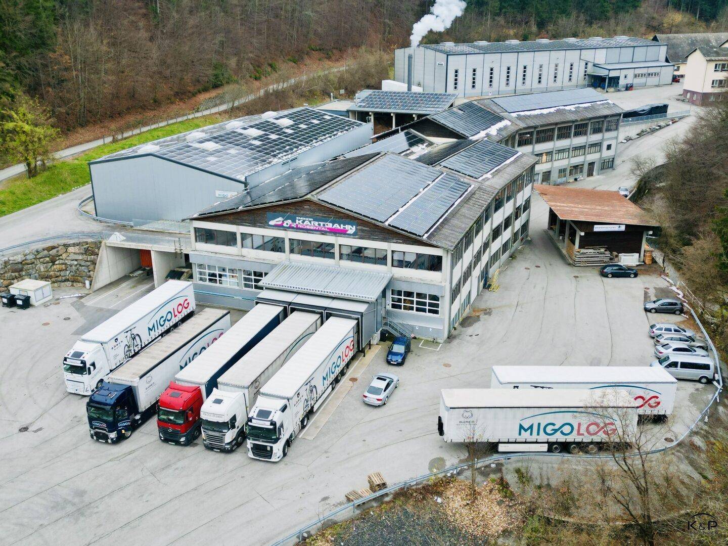 Industriekomplex mit mehreren Gebäuden, Solaranlagen auf den Dächern und LKW-Laderampen.