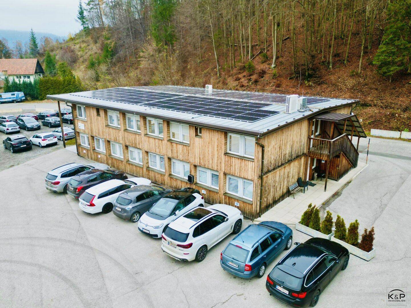 Ansicht des modernen Geschäftsgebäudes mit Holzverkleidung, Solaranlage und angrenzendem Waldgebiet.