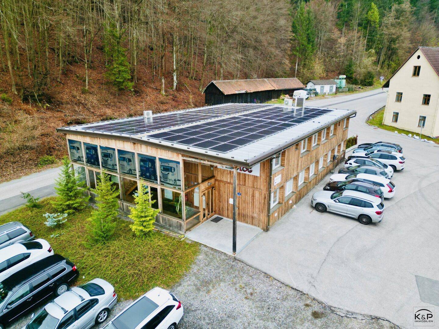 Modernes Geschäftsgebäude mit Holzfassade, Solarpaneelen auf dem Dach und Parkplätzen im Grünen.