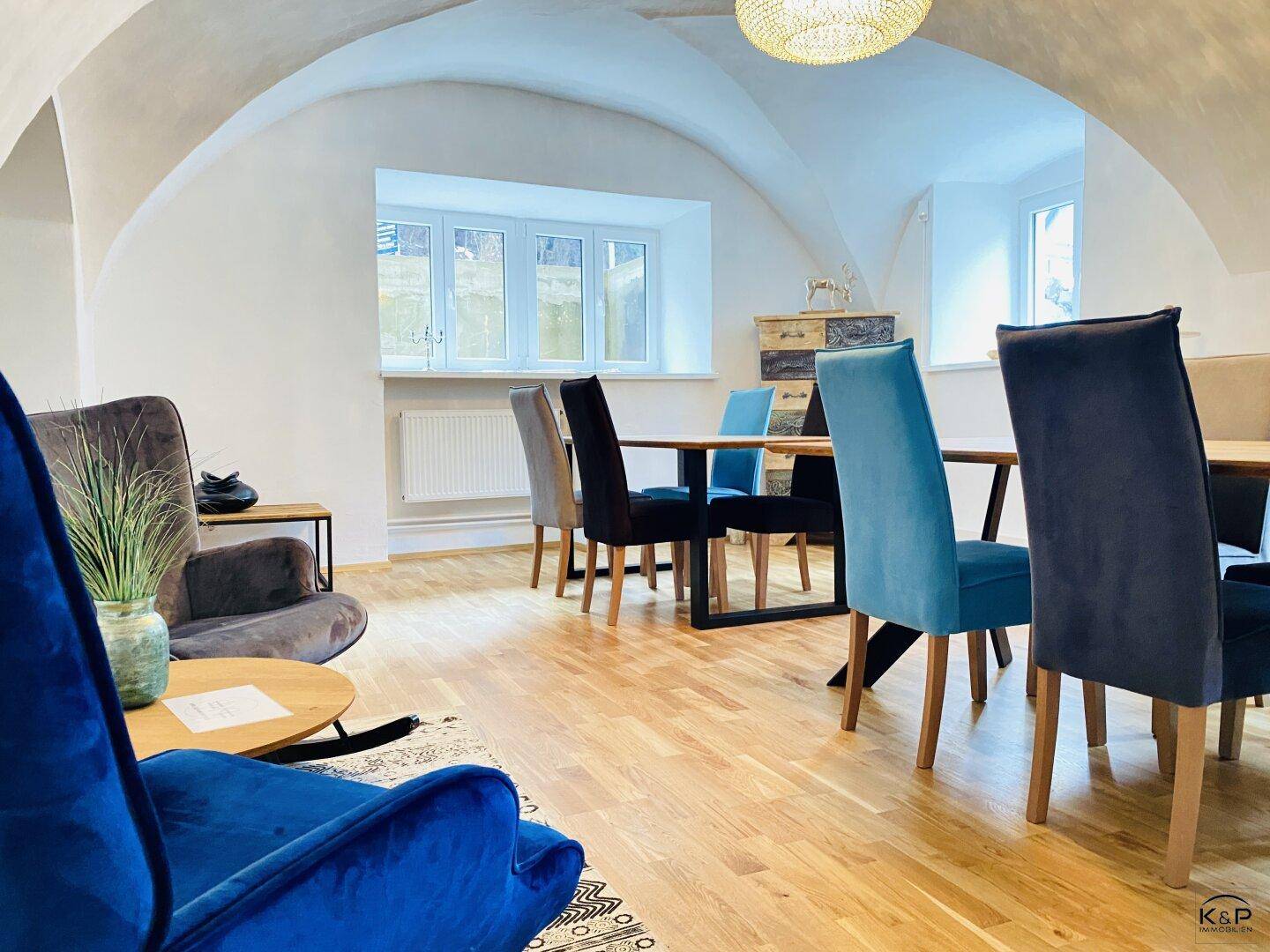 Gemütlicher Ess- und Loungebereich mit gewölbter Decke, Holzboden und modernen blauen Stühlen.