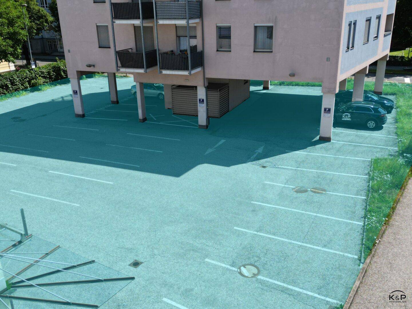 Detailansicht der überdachten Parkplätze unter dem Gebäude mit markierten Stellflächen und geparkten Fahrzeugen.