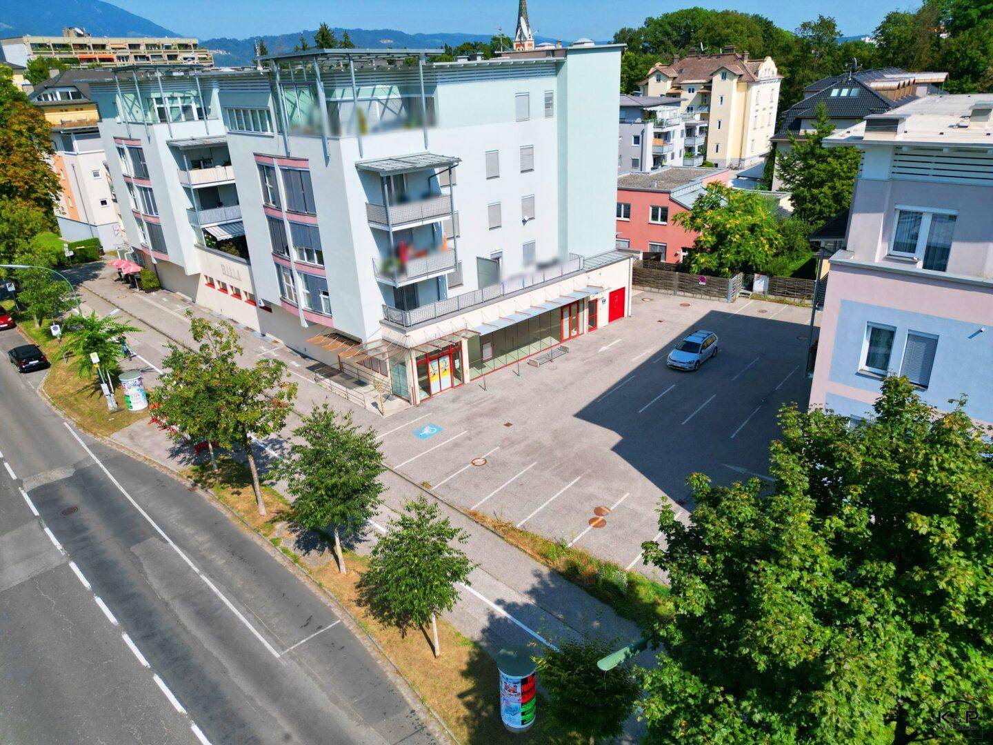 Straßenansicht des modernen Gebäudes mit Ladenflächen im Erdgeschoss und angrenzenden Außenparkplätzen.
