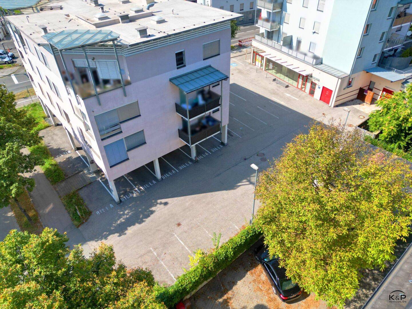 Nahaufnahme aus der Luft des Gebäudes mit überdachten Parkplätzen und angrenzender Grünfläche.