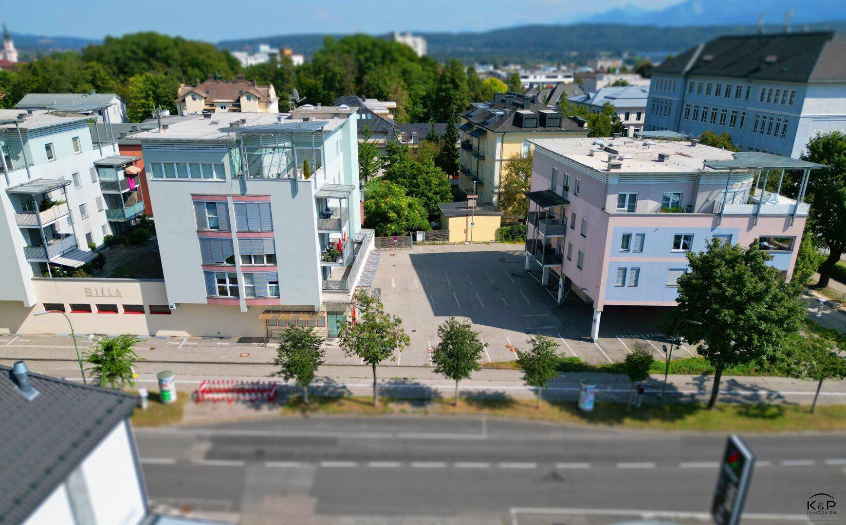 Erhöhte Straßenansicht der beiden modernen Gebäude mit dem dazwischenliegenden Parkplatz und der Hauptstraße.