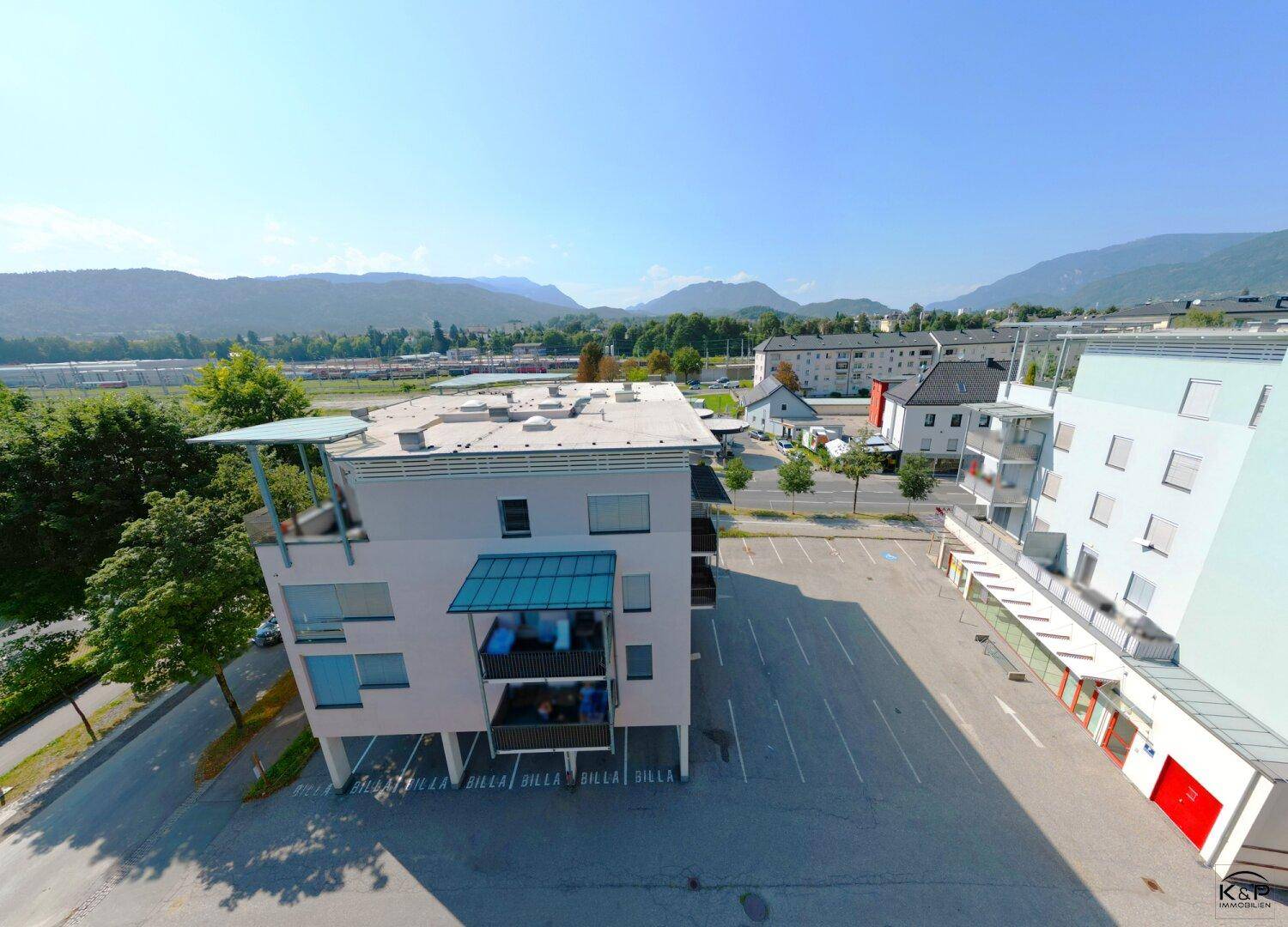 Luftaufnahme des Gebäudes mit großem Parkplatz, umgeben von Bäumen und einer malerischen Bergkulisse.
