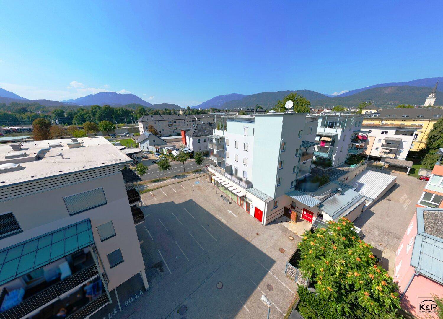 Weitwinkel-Luftaufnahme des Gebäudekomplexes mit Parkplätzen, umgeben von Bäumen und einer beeindruckenden Bergkulisse.
