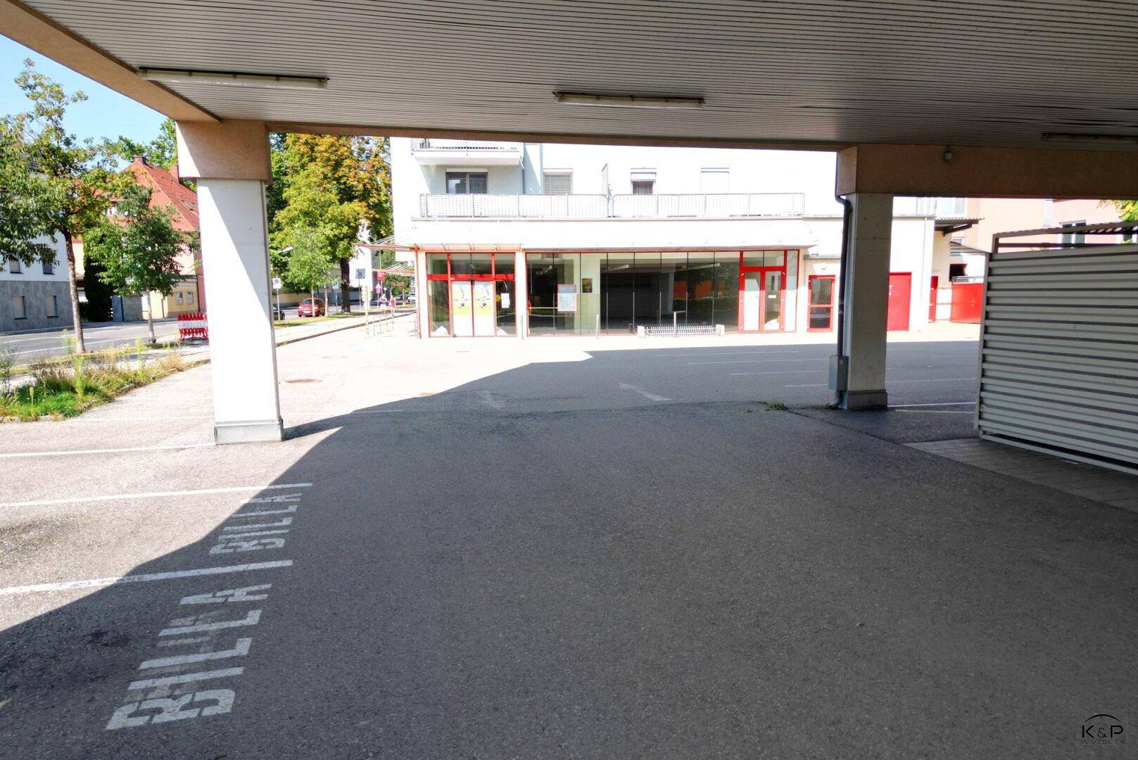 Blick von den überdachten Parkplätzen auf die Ladenfront eines Supermarktes mit großen Schaufenstern.