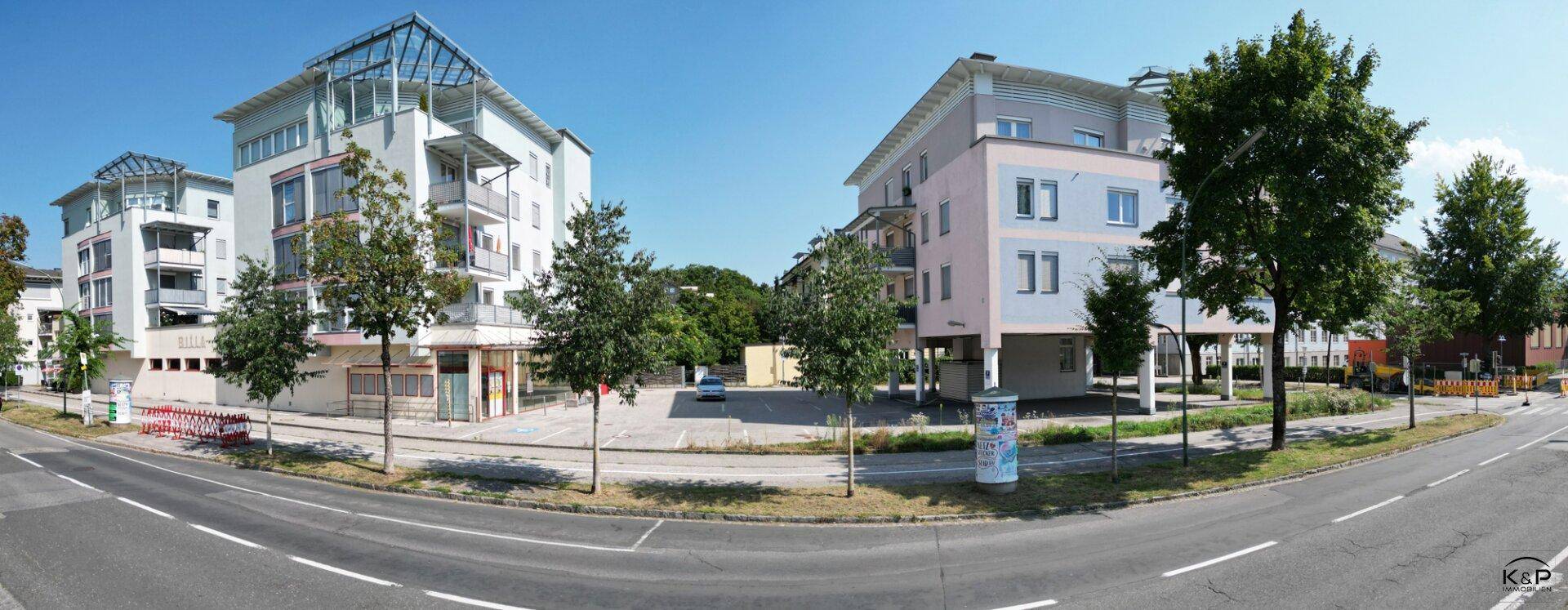 Panoramaansicht der modernen Gebäude von der Straße aus, umgeben von Bäumen und mit Parkmöglichkeiten.