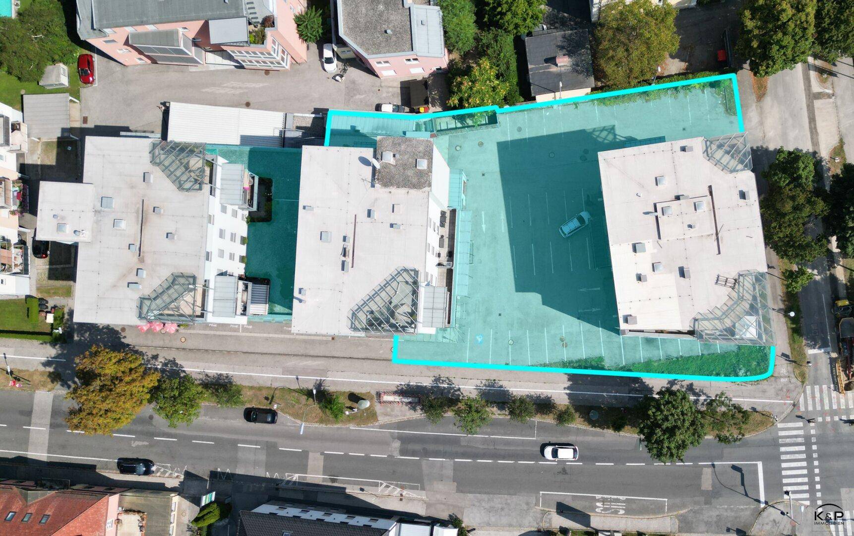 Vogelperspektive des Gebäudekomplexes mit großem Parkplatz und den Dächern der umliegenden Gebäude.