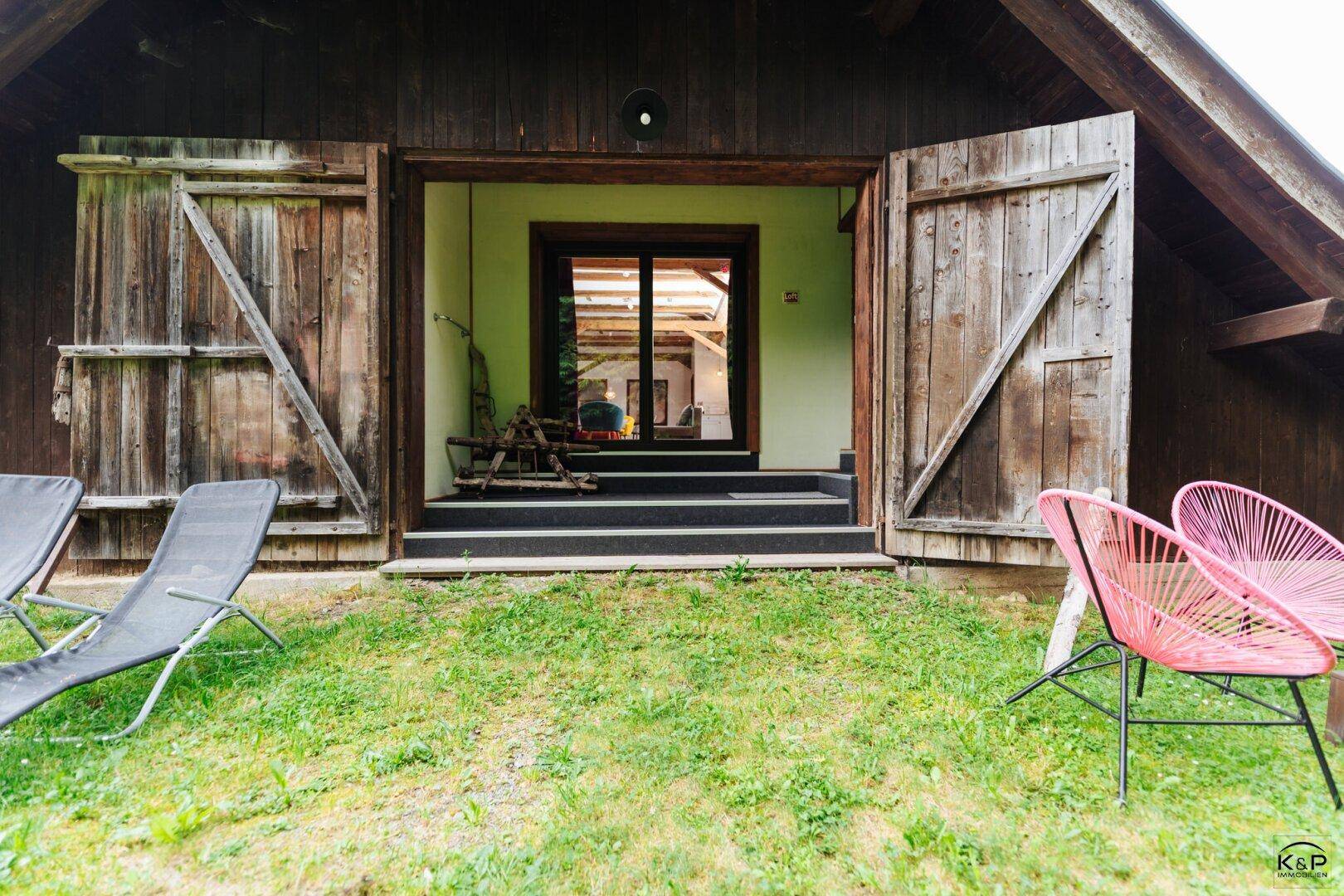 Rustikales Holzgebäude mit großen Scheunentoren und einer kleinen Rasenfläche davor.