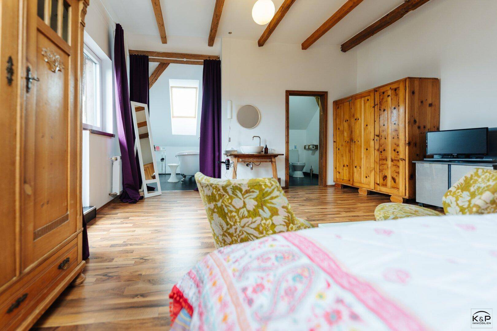 Geräumiges Schlafzimmer mit Holzboden, freiliegenden Balken und offenem Zugang zum Badezimmer.