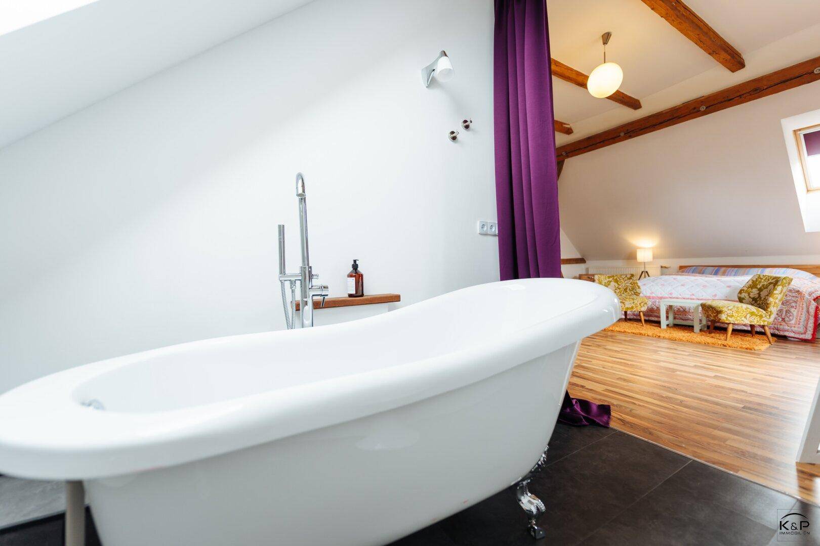 Modernes Badezimmer mit freistehender Badewanne und Blick auf das angrenzende Schlafzimmer.