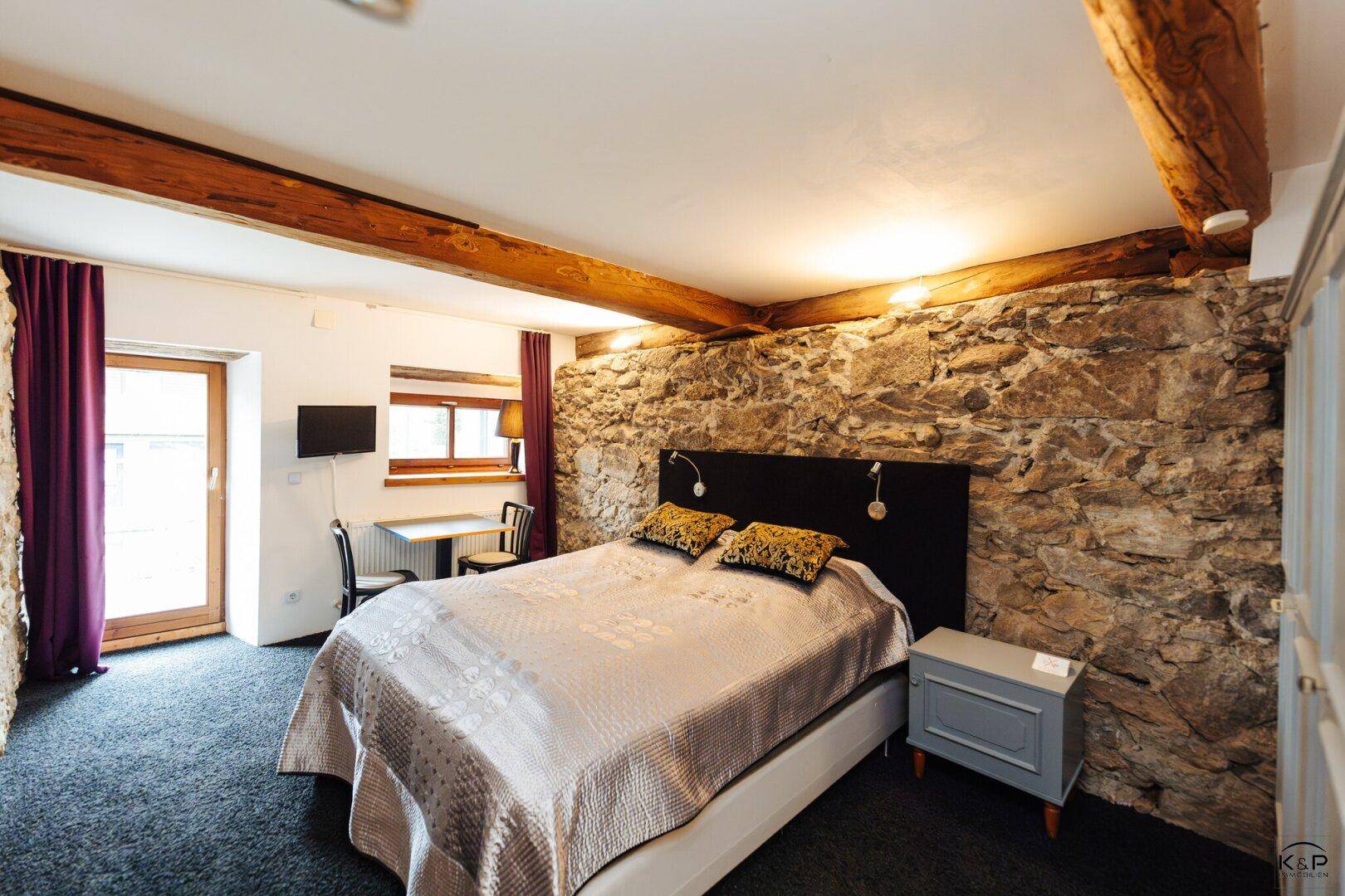 Schlafzimmer mit rustikaler Steinwand, Holzbalken und gemütlicher Atmosphäre.