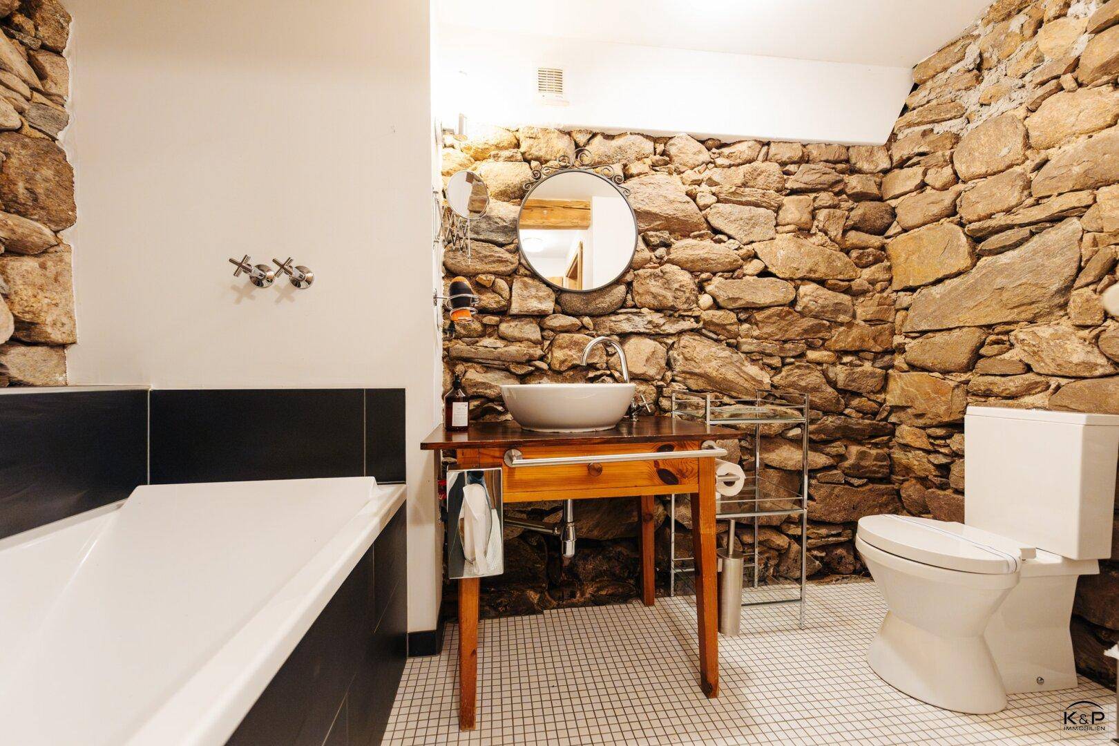 Badezimmer mit rustikaler Steinwand, modernem Waschbecken und weißer Toilette.