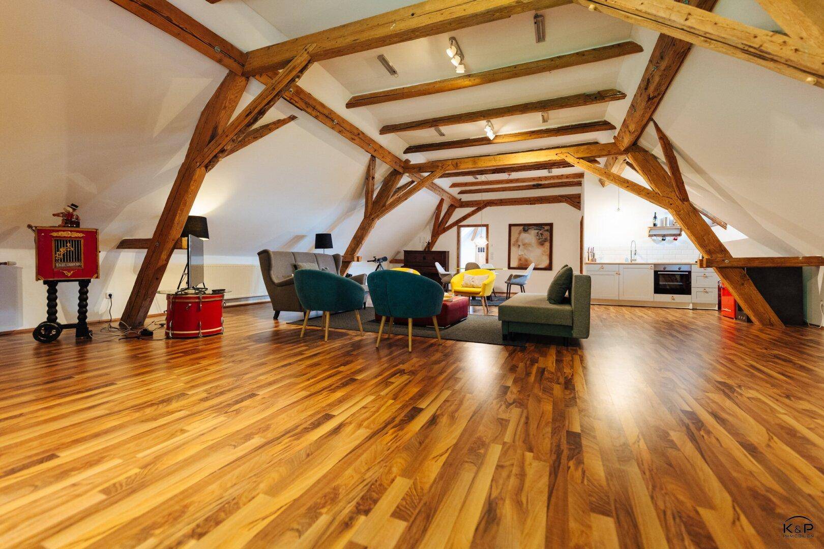 Geräumiger offener Wohnbereich mit Holzbalken, Holzboden und moderner Einrichtung.