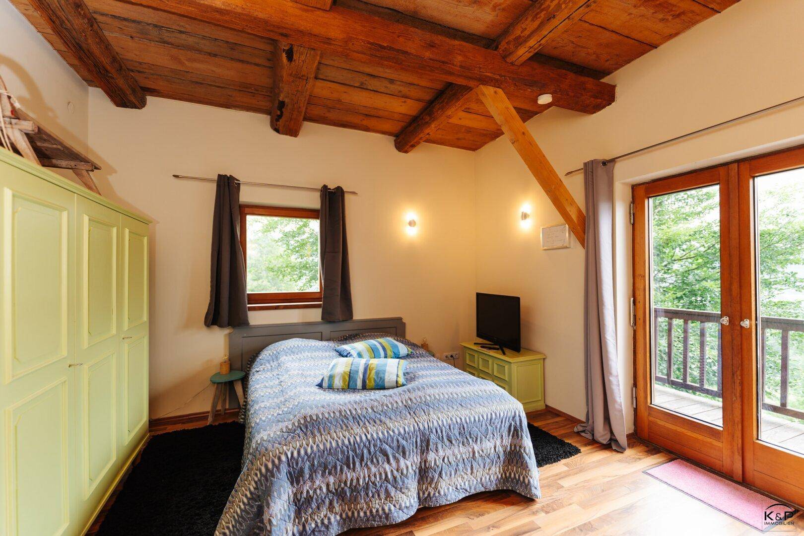 Schlafzimmer mit Holzbalkendecke, Balkonzugang und Blick ins Grüne.