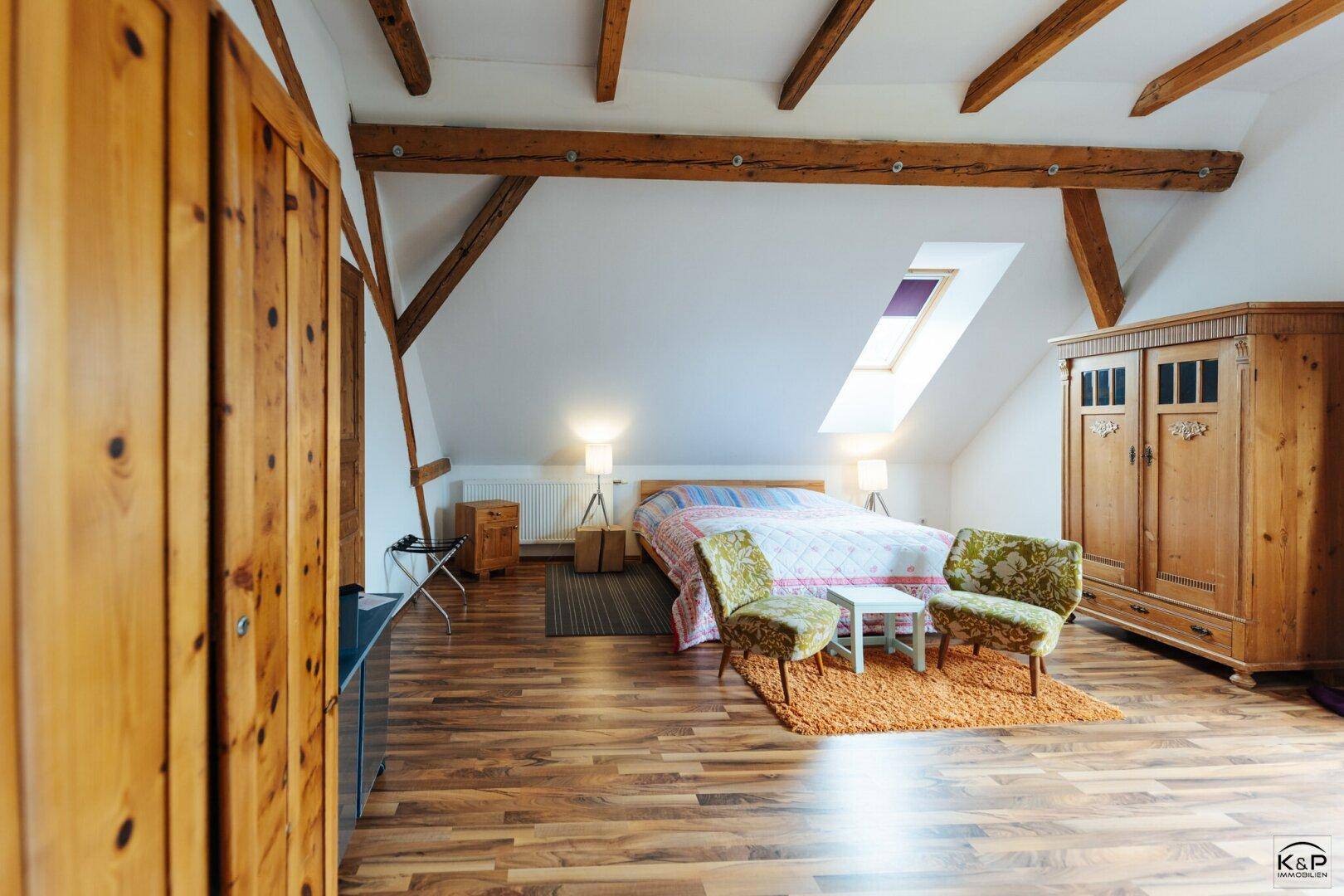 Helles Schlafzimmer mit Holzbalken, Dachfenster und traditionellen Holzmöbeln.