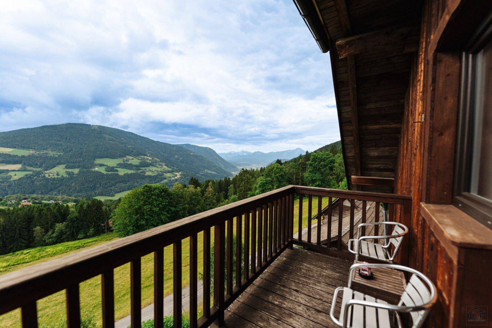 Holzbalkon mit Sitzgelegenheiten und weitem Blick auf die grüne Berglandschaft.