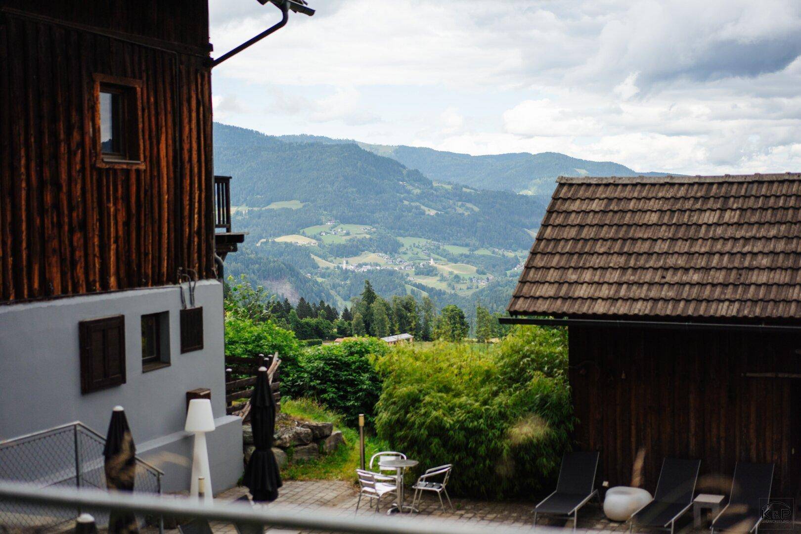 Außenbereich mit Liegestühlen und Sonnenschirmen, umgeben von Natur und Bergblick.