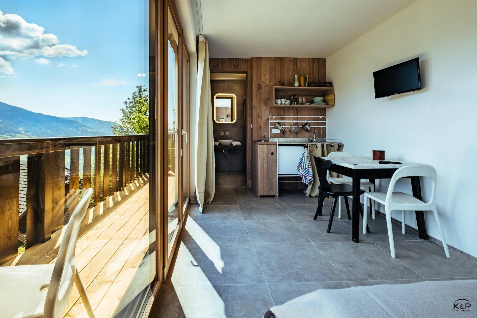 Helles Studio-Apartment mit Balkonzugang, kleiner Küchenzeile und Essbereich mit Bergblick.