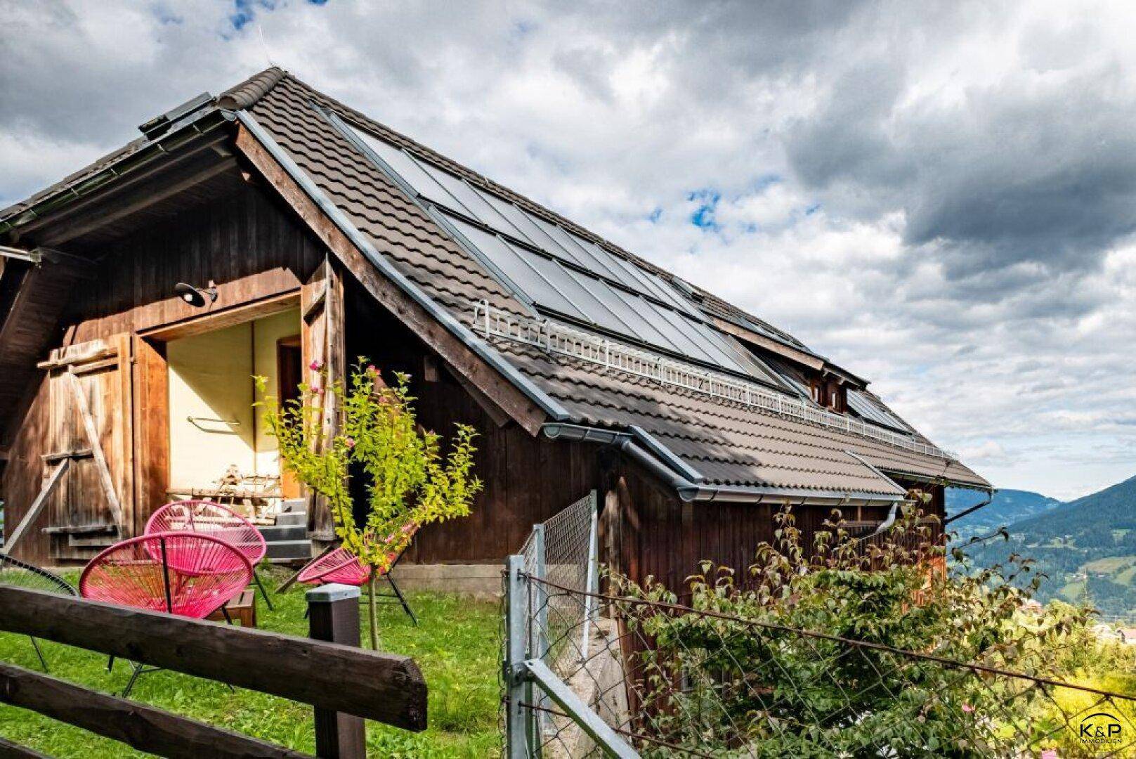 Traditionelles Holzhaus mit Ziegeldach und Photovoltaikanlage auf dem Dach in ländlicher Umgebung.
